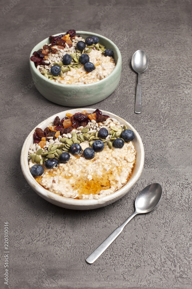 Two bowls of porridge with blueberries, dried fruit and seeds with maple syrup Two bowls of porridge with blueberries, dried fruit and seeds with maple syrup