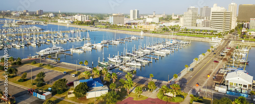 Panorama aerial view waterfront harbor Corpus Christi with marina and downtown skylines in background. Yacht, sailboat is moored at the quay. Top pier speedboat in marina lot filled full row of boat