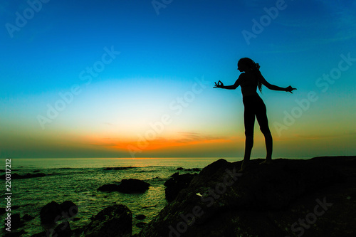 Fitness woman silhouette on the sea during surreal sunset.