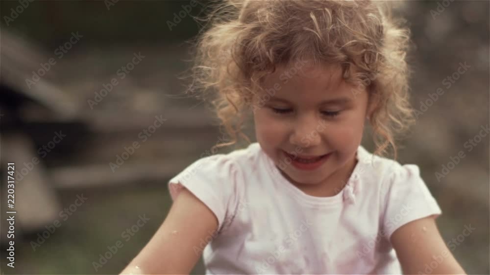 A beautiful little blonde girl with curly hair splashing water into the camera and smiles. Slow motion at 100fps A beautiful little blonde girl with curly hair splashing water into the camera and smiles. Slow motion at 100fps