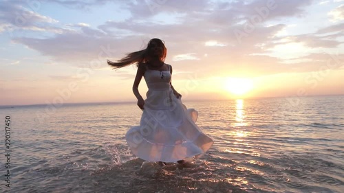 young woman in sundress spinning in the water on the shore photo