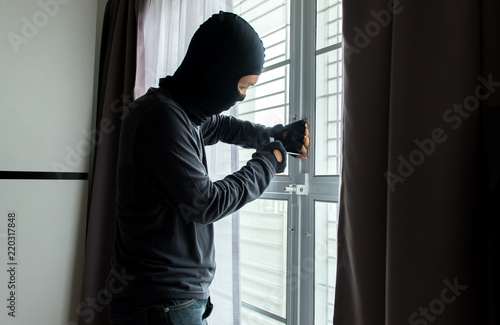 A man burglar in black mask open the door stealing something from house