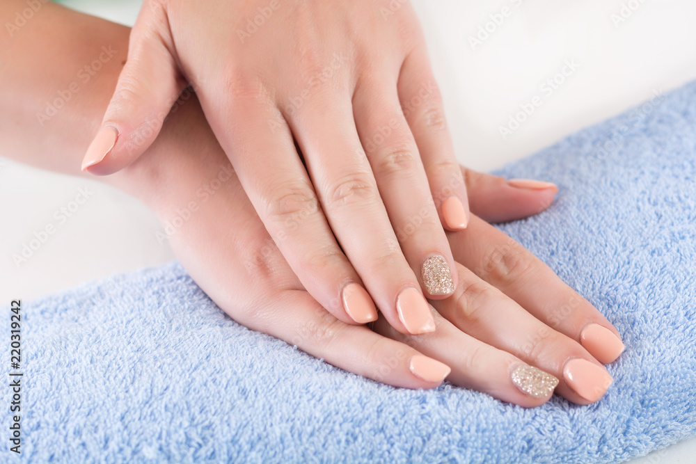 Young woman fingers with orange manicure on nails holding hand on blue towel in beauty studio. Close up, selective focus