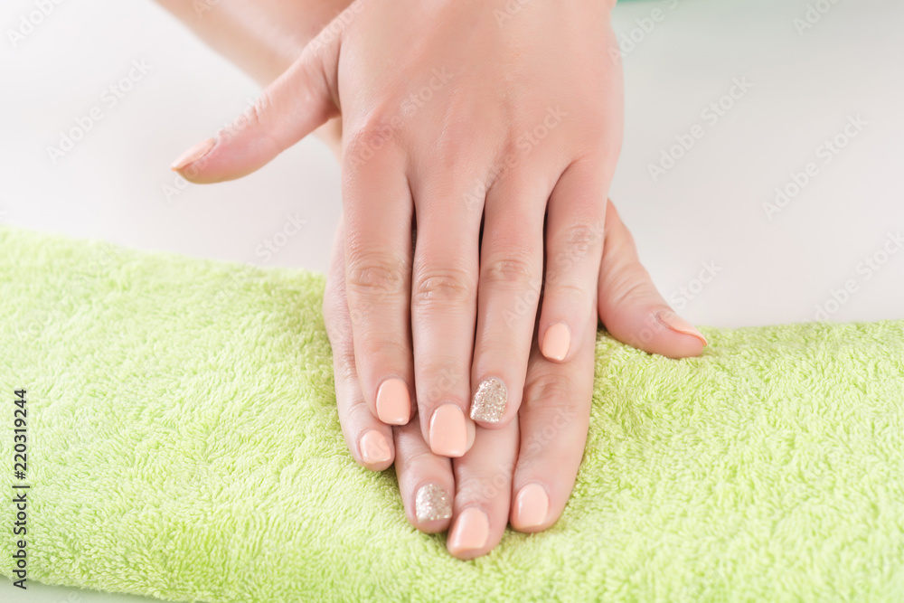 Beautiful woman hands with orange manicure on finger nails on green towel in beauty studio. Close up, selective focus