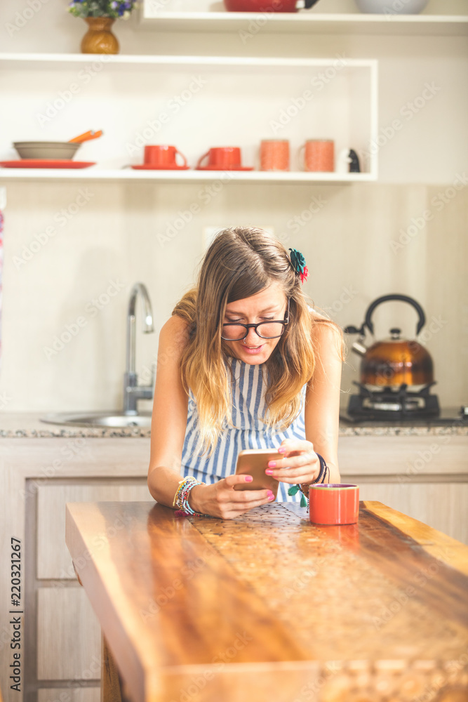 Young woman using cellphone and drinking coffee / tea in a modern kitchen. Young woman using cellphone and drinking coffee / tea in a modern kitchen.