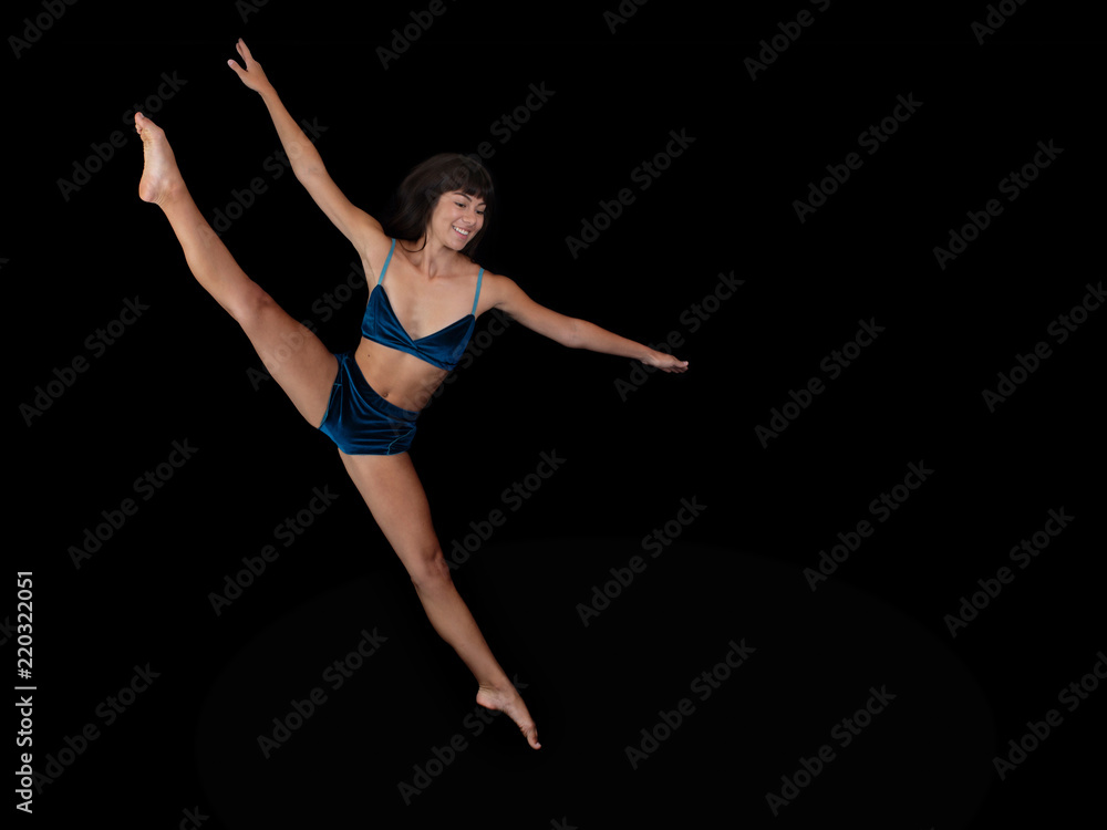 Ballet female dancer with a smile performing a leap on stage with a black backdrop