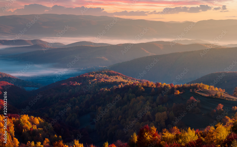 gorgeous red sunrise in mountains. forested hills in colorful fall foliage. fog in the distant valley