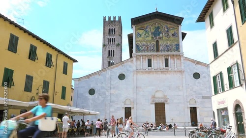 Sightseeing bike tour of Italian landmarks, tourists travel to Tuscany. People walking and taking picture in front of San Frediano church, Lucca, ancient monument of Europe