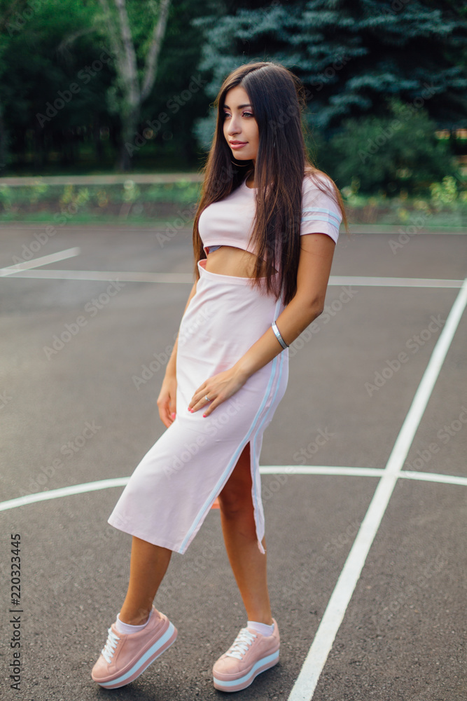 Charming brunette female dressed in a pink dress posing on the basketball court. Charming brunette female dressed in a pink dress posing on the basketball court.