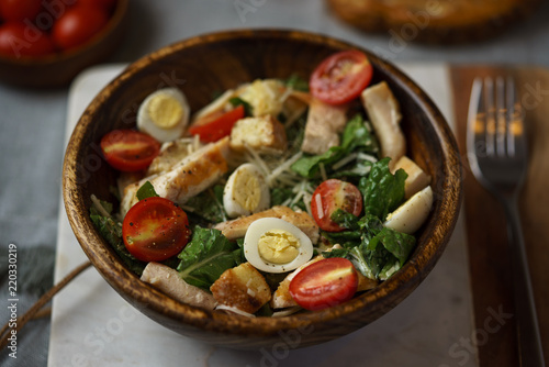 Caesar salad with grilled chicken in wooden bowl