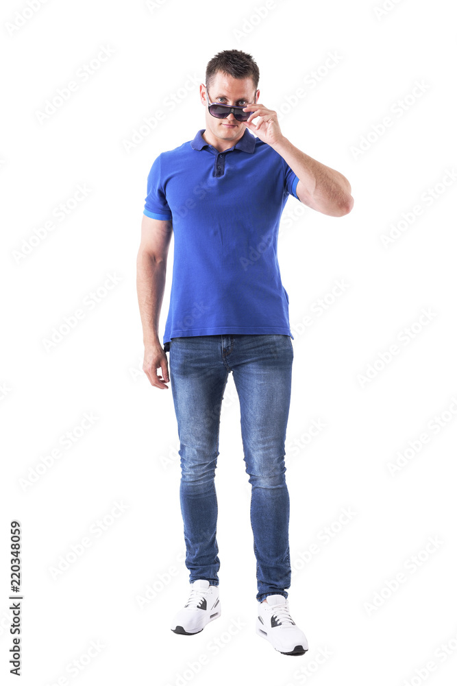 Serious confident young casual man holding sunglasses with over the glasses look at camera. Full body isolated on white background. Serious confident young casual man holding sunglasses with over the glasses look at camera. Full body isolated on white background.