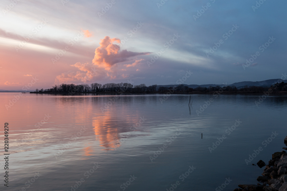A shoot of a sunset over a lake, with beautiful warm colors and clouds and perfectly symmetryc reflections