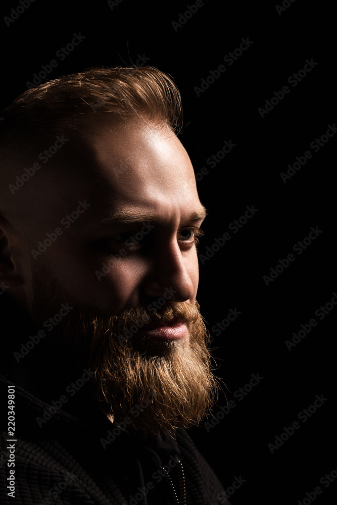 Fototapeta premium male portrait of a guy with a beard on a black background close-up