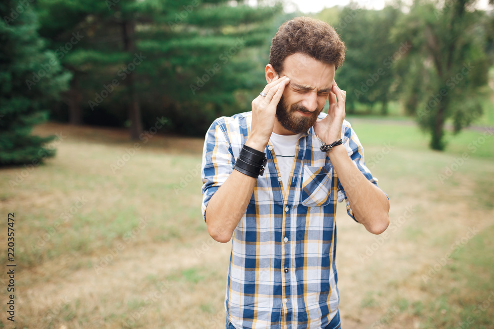 Young bearded hipster got sick and headache in the park. Young bearded hipster got sick and headache in the park.