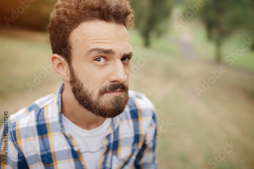 Attractive curious young bearded hipster posing in the park.
