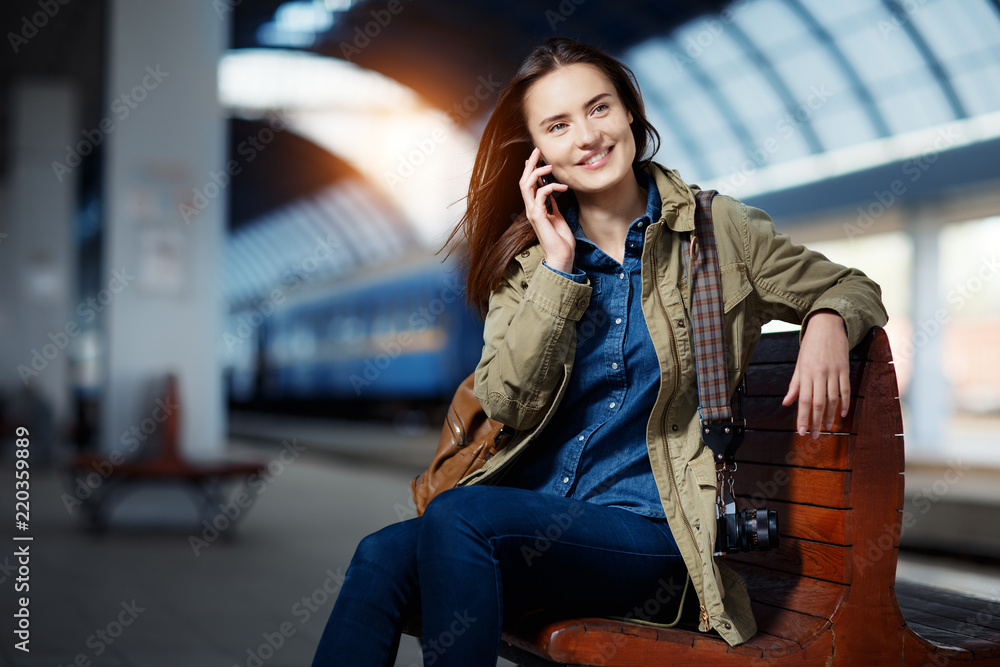 Woman talking on smartphone while sitting on the bench on the railway station platform. Woman talking on smartphone while sitting on the bench on the railway station platform.