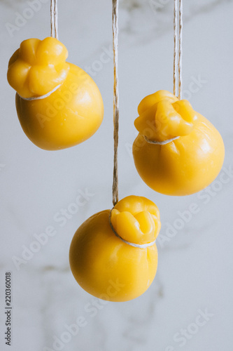 Scamorza cheeses are hanged together in strings to ripen on marble background