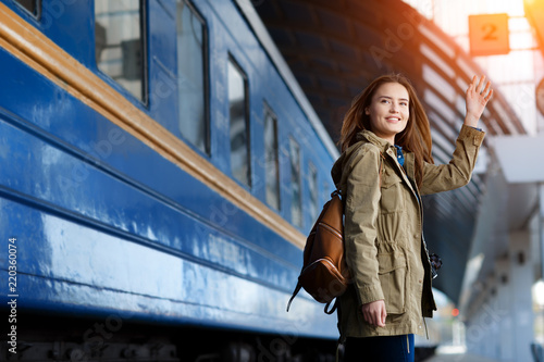 Happy young woman waitng train on the railway station platform. Woman travel with the train. photo