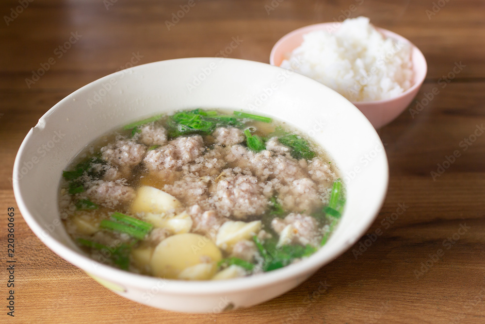 A Bowl of Minced pork and soya bean curd soup with a cup of Steamed rice. Put on  wooden table.