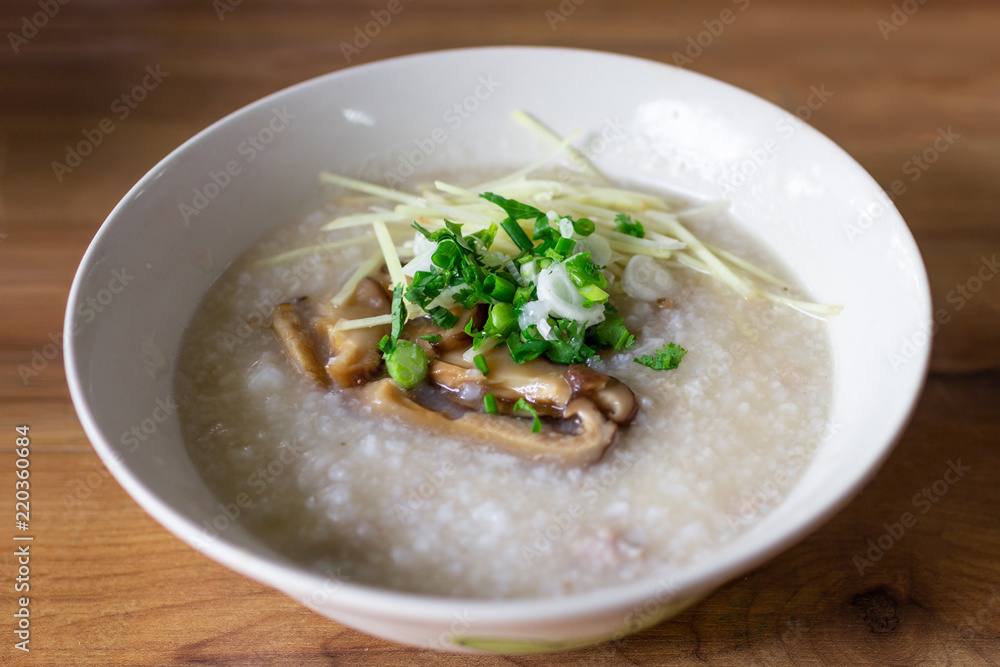 A bowl of Congee with minced pork sprinkle with mushroom, ginger, spring onion and coriander. Put on wooden table. A bowl of Congee with minced pork sprinkle with mushroom, ginger, spring onion and coriander. Put on wooden table.