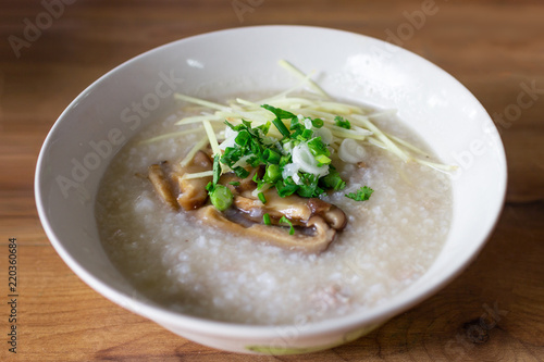 A bowl of Congee with minced pork sprinkle with mushroom, ginger, spring onion and coriander. Put on wooden table.