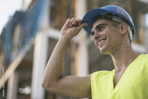 Fotografie Smiling latino or caucasian dark haired construction worker touching his hardhat