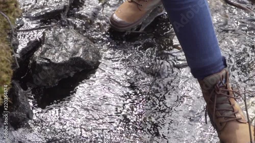 Woman with boots and jeans carefully crossing over a small stream from a waterfall photo