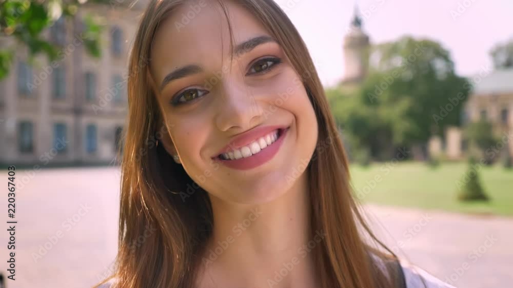 Sexy woman is standing in park in daytime, watching at camera, smiling, blurred background Sexy woman is standing in park in daytime, watching at camera, smiling, blurred background