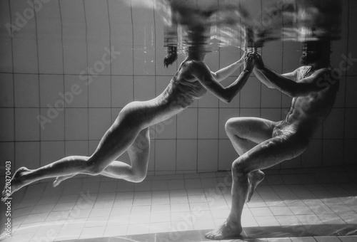 monochrome underwater portrait of the sporty dancing and doing yoga asanas couple underwater in the swimming pool