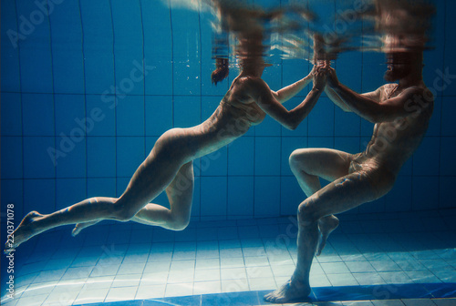 underwater portrait of the atlethic, sporty dancing and doing yoga asanas couple (man and woman) underwater in the swimming pool