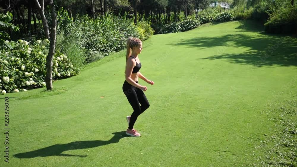 Young blond woman with a slender figure is engaged in gymnastics at public park. She makes a run in place fitness exercise. Slow motion Young blond woman with a slender figure is engaged in gymnastics at public park. She makes a run in place fitness exercise. Slow motion