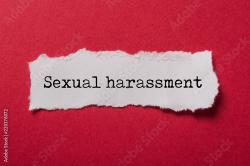 closeup of white torn paper on red paper background with text - Sexual harassment