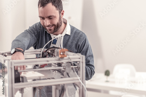 New technology. Smiling bearded man testing new 3D printer learning how to work with it