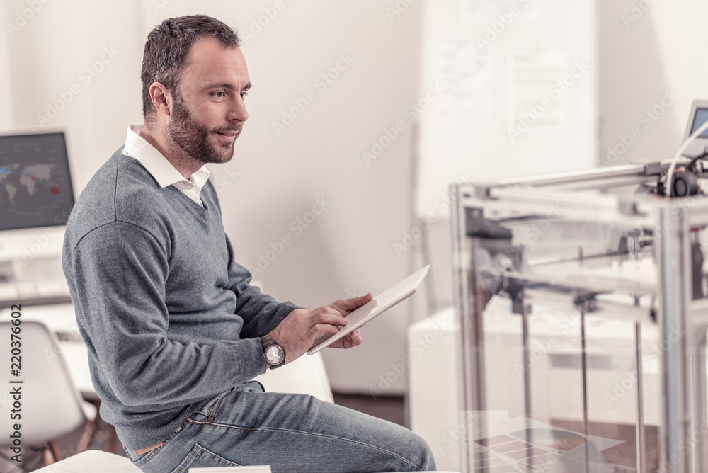 Professional worker. Professional smart man directing printer by his tablet sitting at the office
