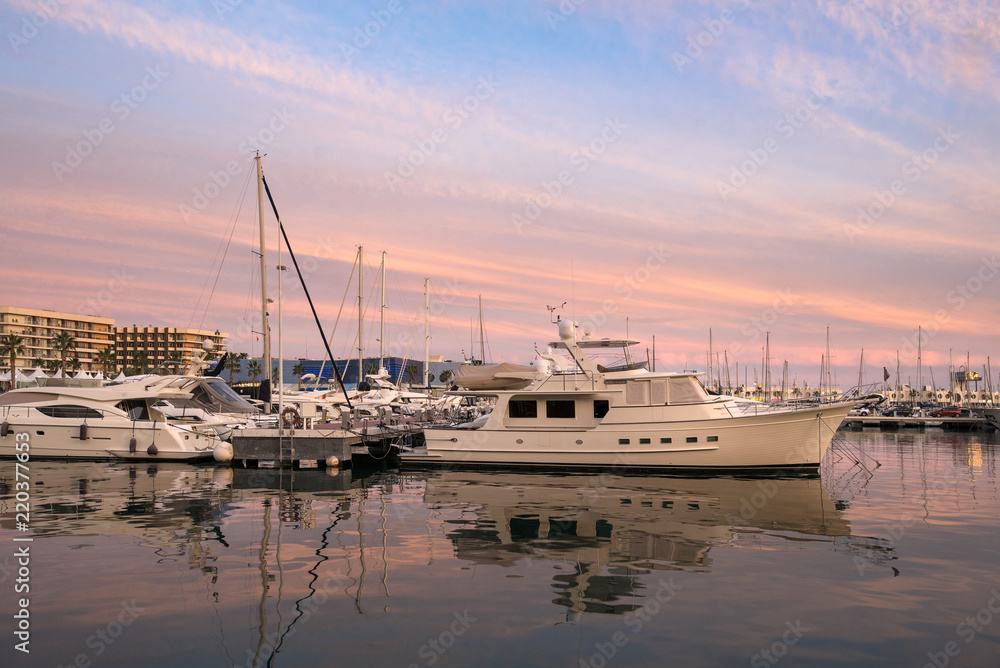 Fototapeta premium Beautiful port of Alicante, Spain at Mediterranean sea. Luxury yachts, ships, ferries and fishing boats sailing and standing in rows in harbor. Rich people traveling around the world. Sunset evening