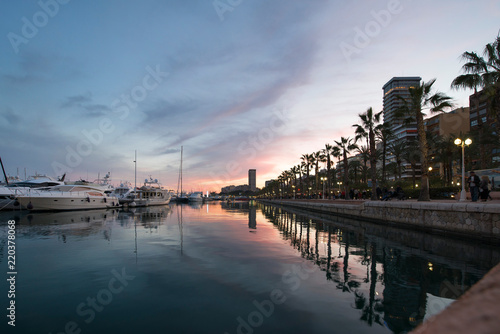 Beautiful port of Alicante, Spain at Mediterranean sea. Luxury yachts, ships, ferries and fishing boats sailing and standing in rows in harbor. Rich people traveling around the world. Sunset evening © lainen