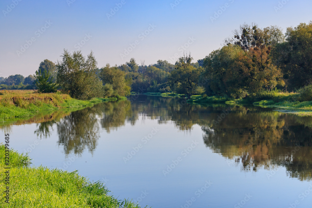 Calm surface of the river against blue sky at summer morning. River landscape at sunrise