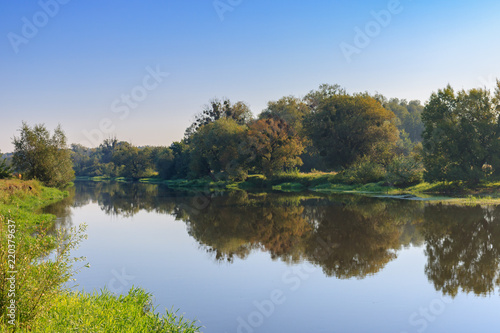 Fototapeta Naklejka Na Ścianę i Meble -  River landscape in sunny summer morning on a background of green trees on the shore