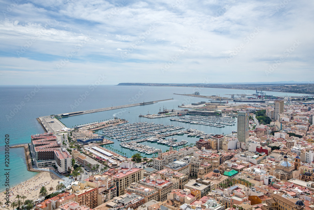 Beautiful port of Alicante, Spain. Luxury yachts, ships and fishing boats sailing and standing in rows in harbor. Palm trees at coastline and vibrant blue water. Sunny day at Mediterranean sea. 
