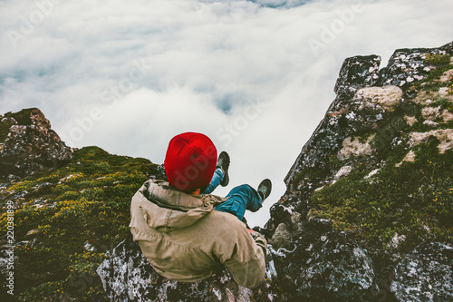 Man relaxing sitting alone on cliff edge rocky mountains above clouds travel adventure lifestyle extreme vacations