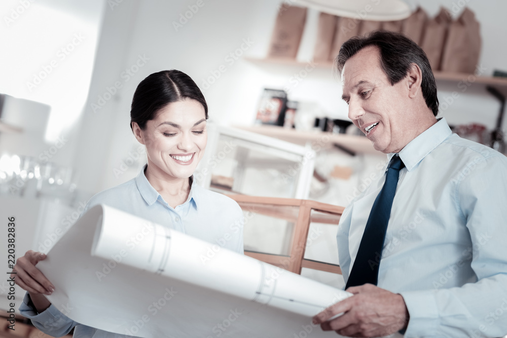 Fototapeta premium New scheme. Two professional architects standing with a big scheme and smiling while looking at it