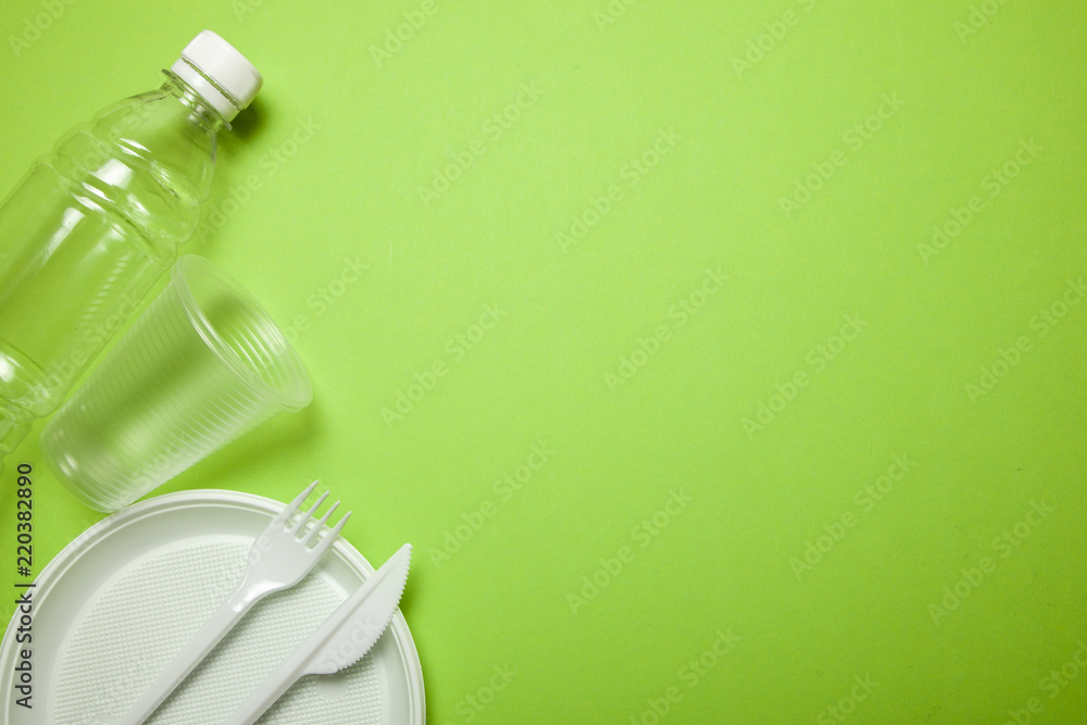 Plastic disposable utensils on green. fork, knives, plates, cups and bottle Plastic disposable utensils on green. fork, knives, plates, cups and bottle