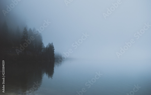 Mysterious mountain lake in early spring morning. Spooky dense fog covering the water. Sleepy misty landscapes in Alps, Austria.