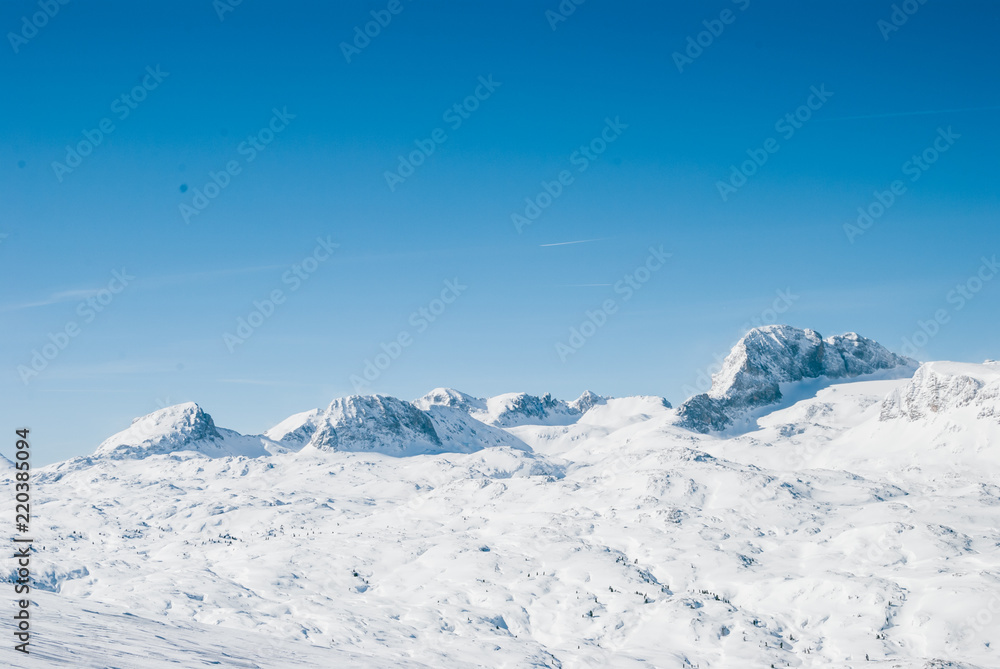 Snowy winter landscape in the Austrian Alps. Rocky plateau covered by sunlight. Bright white light reflected by snow