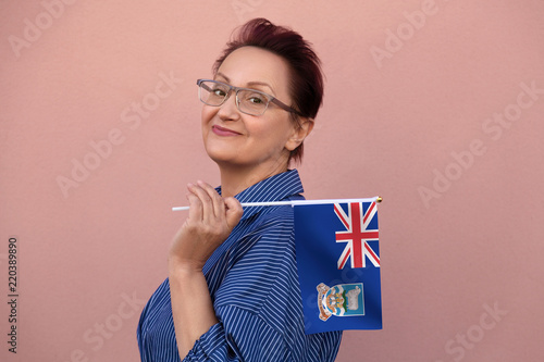 Falkland Islands flag. Woman holding Falkland Islands flag. Nice portrait of middle aged lady 40 50 years old with a national flag over pink wall on the street outdoors. photo