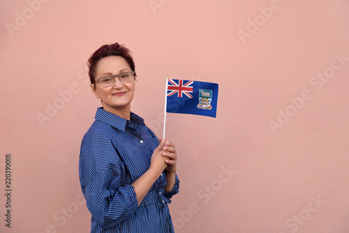 Falkland Islands flag. Woman holding Falkland Islands flag. Nice portrait of middle aged lady 40 50 years old with a national flag over pink wall on the street outdoors. photo