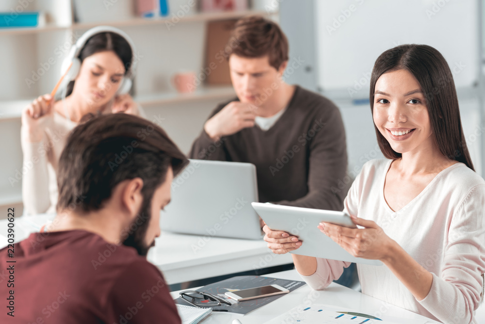 Modern students. Positive Asian student smiling while using a tablet Modern students. Positive Asian student smiling while using a tablet