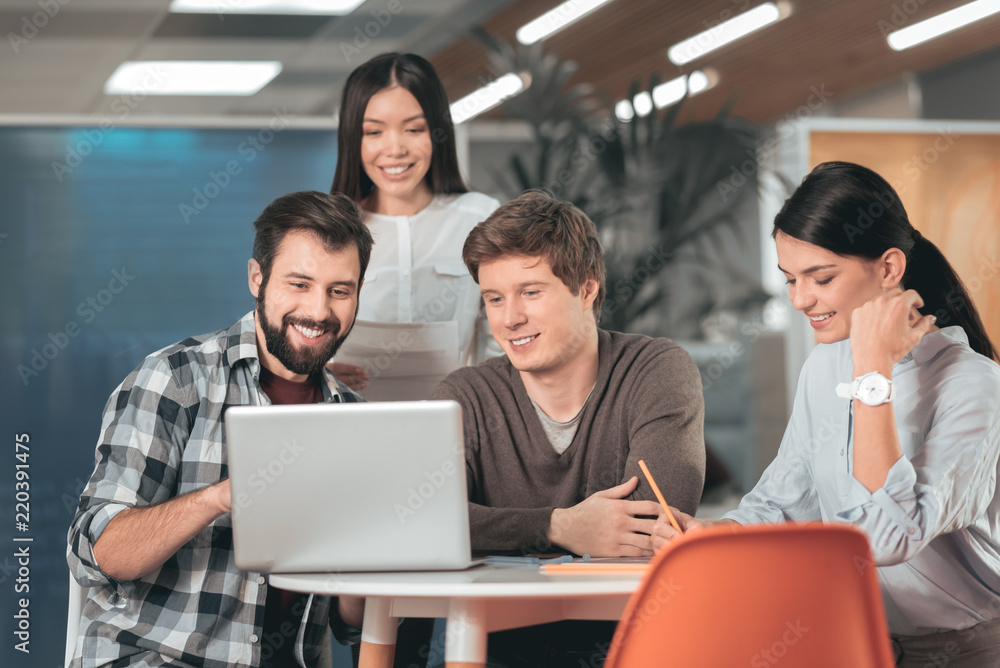 Look at this. Pleasant young man sitting together with his friend while pointing at the laptop screen Look at this. Pleasant young man sitting together with his friend while pointing at the laptop screen