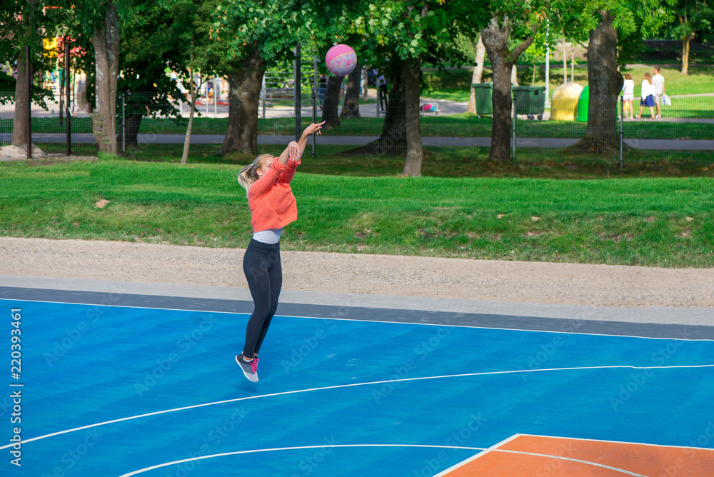 Sport background of girl playing basketball in outdoor basketball court in park. Friends sitting and watching