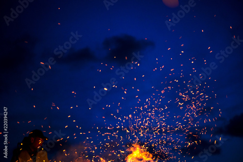 Large burning bonfire with soft glowing flame throws flying sparkles all around. Romantic summer evening, people relaxing and enjoying calmness at the seaside during the Night of ancient lights